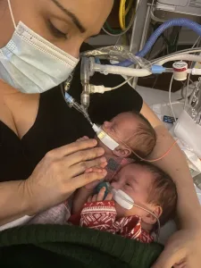 Jaclyn Vasquez wears a mask and holds her twin micro-preemie daughters, Ava and Olivia, in the neonatal intensive care unit 