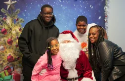 A DSCC participant family of four poses with Santa Claus in front of a festive holiday photo backdrop in DSCC's Mokena Regional Office