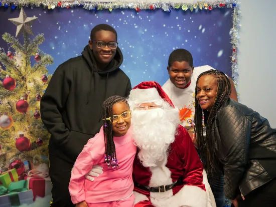 A DSCC participant family of four poses with Santa Claus in front of a festive holiday photo backdrop in DSCC's Mokena Regional Office