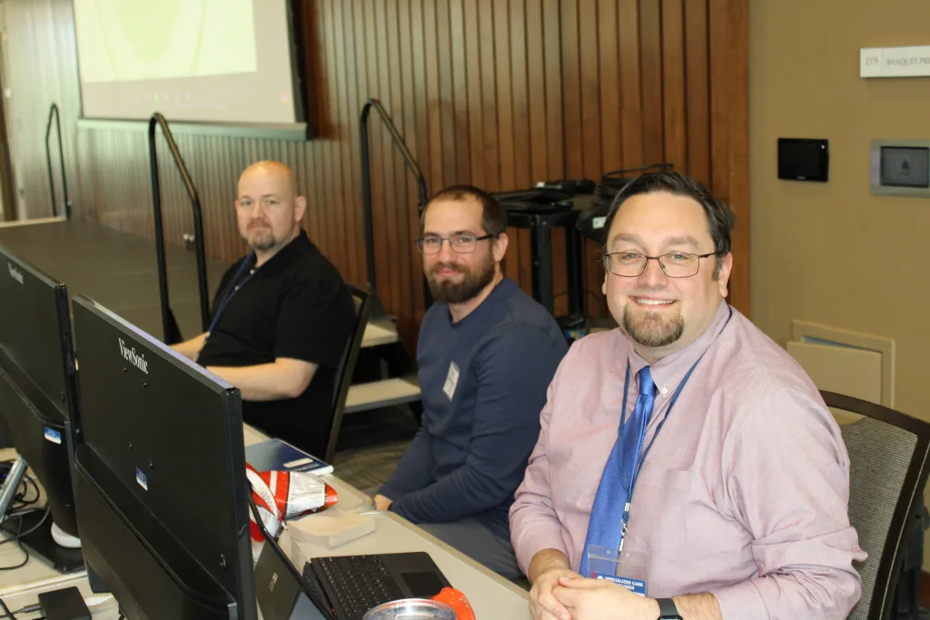 From left to right: Mac Burks, Zack Alumbaugh and Greg Mayes set up an Information Technology desk at the Together Towards Tomorrow Conference in the spring of 2023.