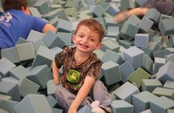 A young Division of Specialized Care for Children participant with a limb difference smiles as he plays in the foam block pit of the Sensory Station at the Illinois State Fair